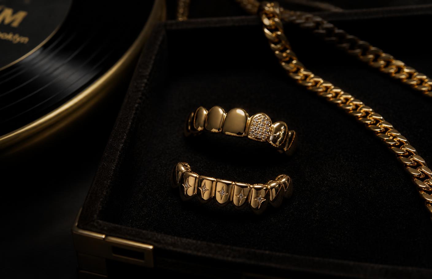 Custom gold oral jewelry in a velvet case beside a gold chain and a record